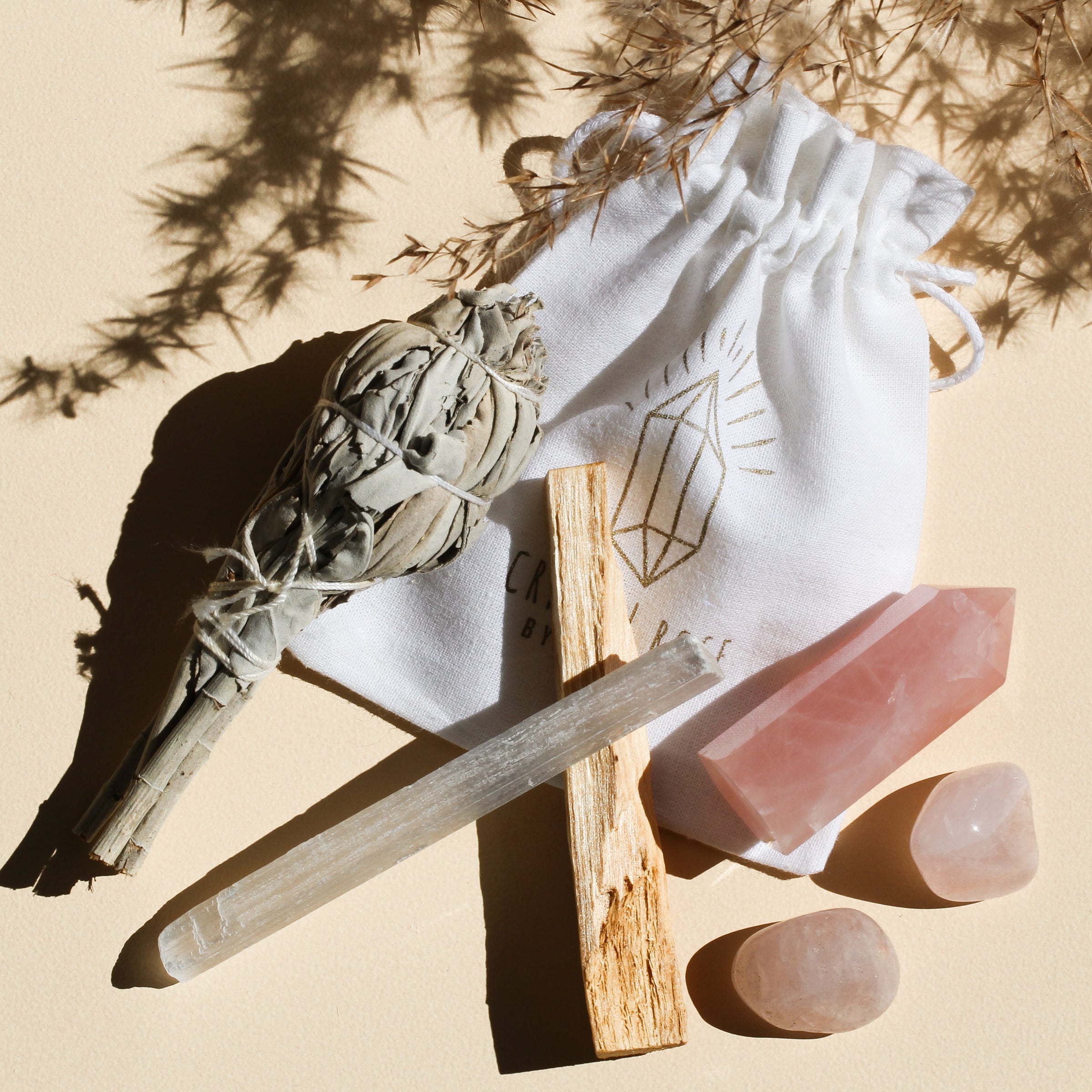 This bundle features a 1 medium Rose Quartz Point (5-6cm), 2 Rose Quartz Tumbles (2-3cm), 1 White Sage stick (10cm long), 1 Selenite stick (10cm long), and 1 Palo Santo stick (10cm), curated for love, cleansing, and protection, including a bag